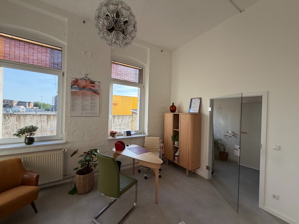 Heller Behandlungsraum mit Schreibtisch und viel Tageslicht
